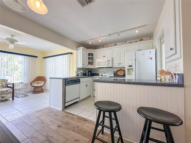 kitchen with white appliances, a breakfast bar, white cabinetry, a textured ceiling, and kitchen peninsula