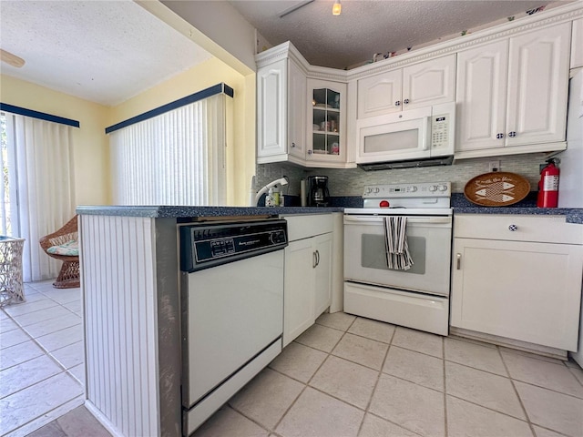 kitchen featuring white appliances, light tile patterned floors, a textured ceiling, and white cabinets