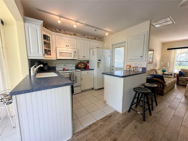 kitchen with white cabinetry, a breakfast bar, sink, and white appliances