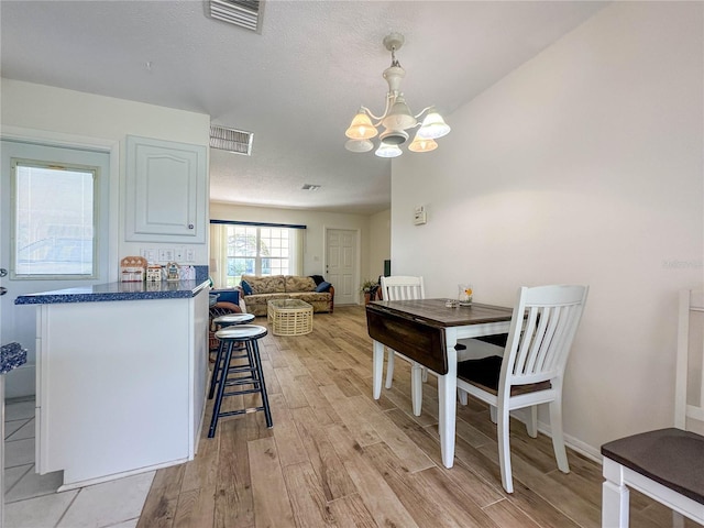 dining room with a textured ceiling, a notable chandelier, and light hardwood / wood-style floors