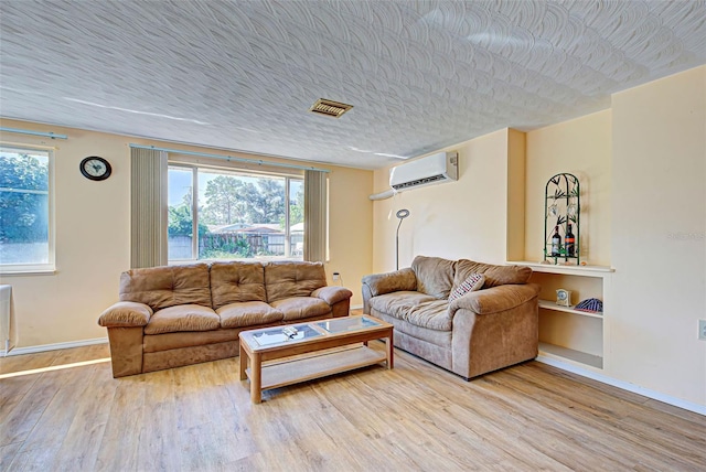 living room with light hardwood / wood-style floors, a wall mounted air conditioner, and a textured ceiling