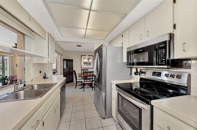 kitchen with decorative light fixtures, light tile floors, appliances with stainless steel finishes, white cabinets, and sink