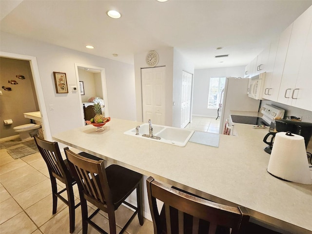 kitchen with light tile patterned flooring, kitchen peninsula, white appliances, a breakfast bar, and white cabinets