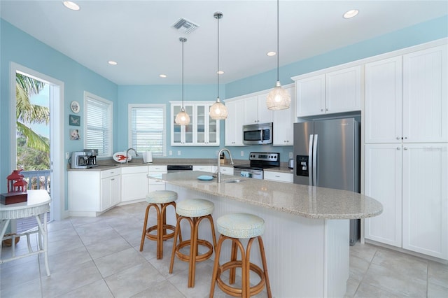 kitchen with pendant lighting, light tile patterned floors, a kitchen island with sink, appliances with stainless steel finishes, and white cabinets