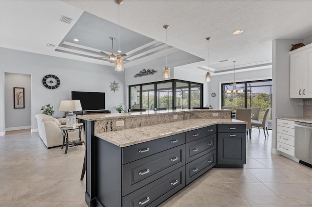 kitchen with a raised ceiling, plenty of natural light, ceiling fan with notable chandelier, and white cabinets