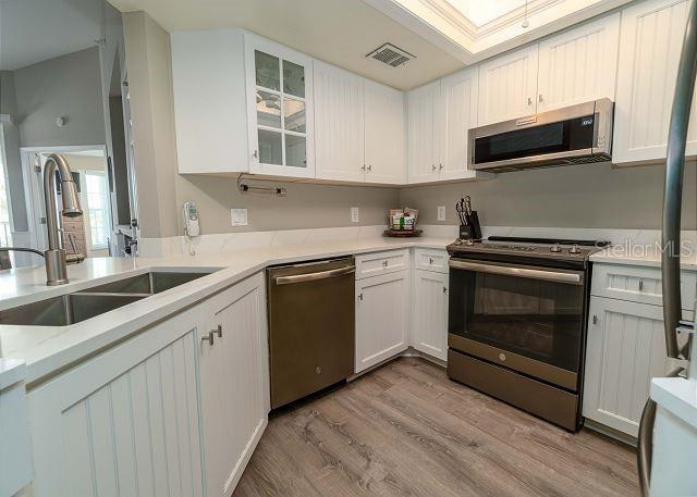 kitchen featuring white cabinetry, appliances with stainless steel finishes, sink, light hardwood / wood-style flooring, and light stone counters