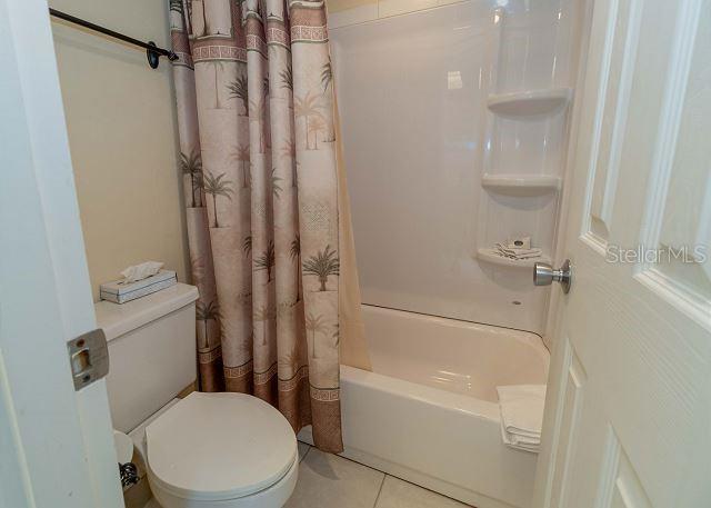 bathroom with toilet, tile flooring, and shower / tub combo with curtain