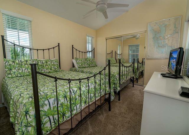 carpeted bedroom with a closet, multiple windows, ceiling fan, and vaulted ceiling