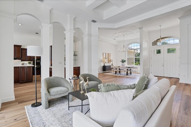 living room featuring ornamental molding, light hardwood / wood-style floors, coffered ceiling, ornate columns, and an inviting chandelier