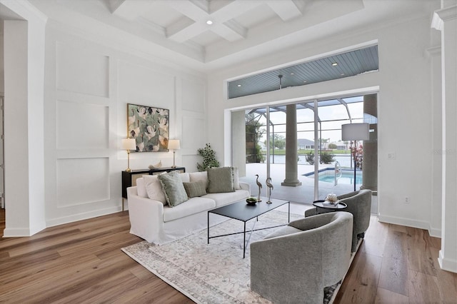 living room featuring beamed ceiling, coffered ceiling, a towering ceiling, and light hardwood / wood-style flooring