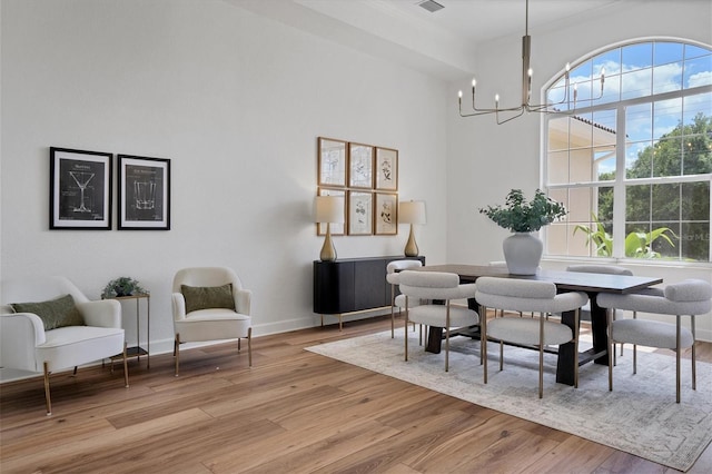 dining room with a high ceiling, an inviting chandelier, a healthy amount of sunlight, and light wood-type flooring