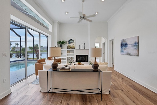 living room with crown molding, a towering ceiling, ceiling fan, and light wood-type flooring