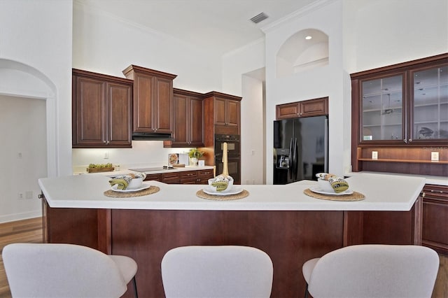 kitchen featuring a kitchen breakfast bar, ornamental molding, dark wood-type flooring, black appliances, and a center island