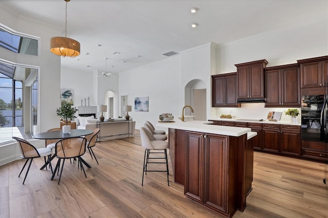 kitchen with black double oven, pendant lighting, dark brown cabinets, a center island with sink, and light hardwood / wood-style floors