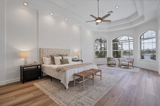 bedroom featuring ceiling fan, a raised ceiling, a towering ceiling, and light wood-type flooring