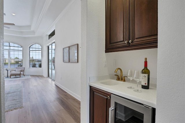 bar with sink, a raised ceiling, dark brown cabinets, light hardwood / wood-style flooring, and wine cooler