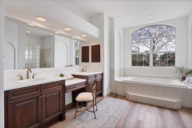 bathroom featuring double vanity, a healthy amount of sunlight, a relaxing tiled bath, and hardwood / wood-style floors