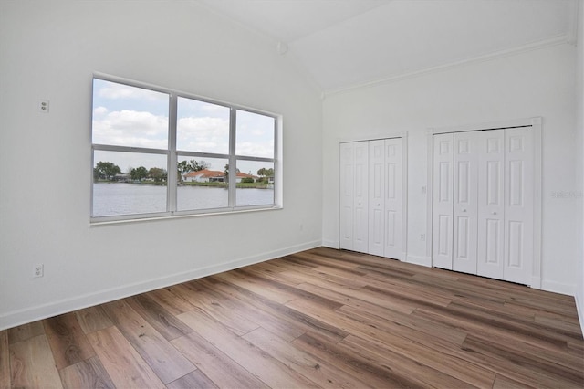 unfurnished bedroom featuring lofted ceiling, dark wood-type flooring, multiple closets, a water view, and crown molding