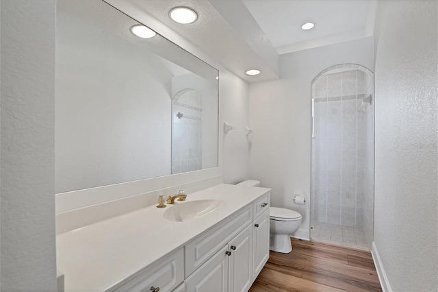 bathroom with hardwood / wood-style floors, vanity with extensive cabinet space, toilet, and tiled shower