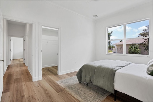 bedroom with a closet, ornamental molding, a spacious closet, and light hardwood / wood-style flooring