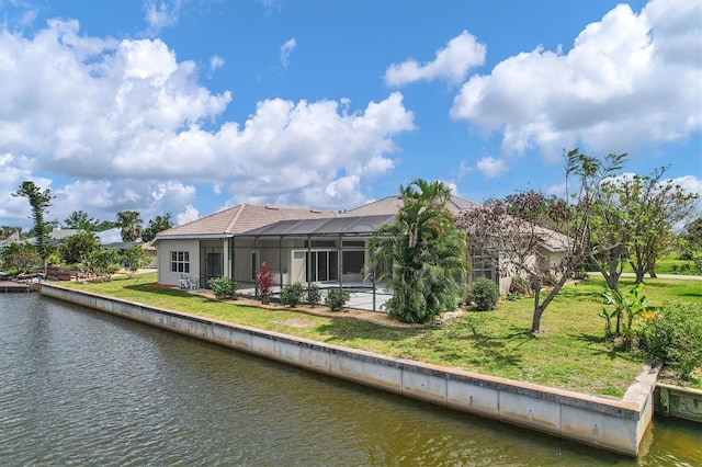 rear view of house with a lawn, a water view, and a lanai