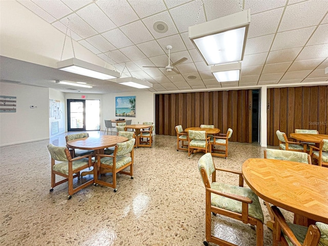 dining room featuring wood walls, ceiling fan, and a paneled ceiling