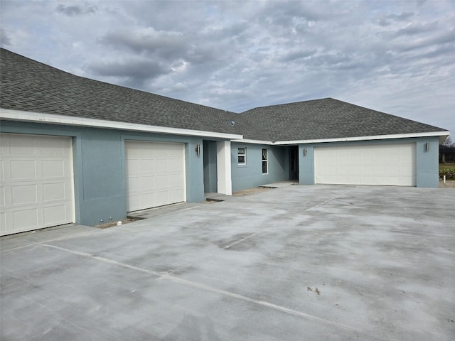 ranch-style home with a garage, a shingled roof, and stucco siding