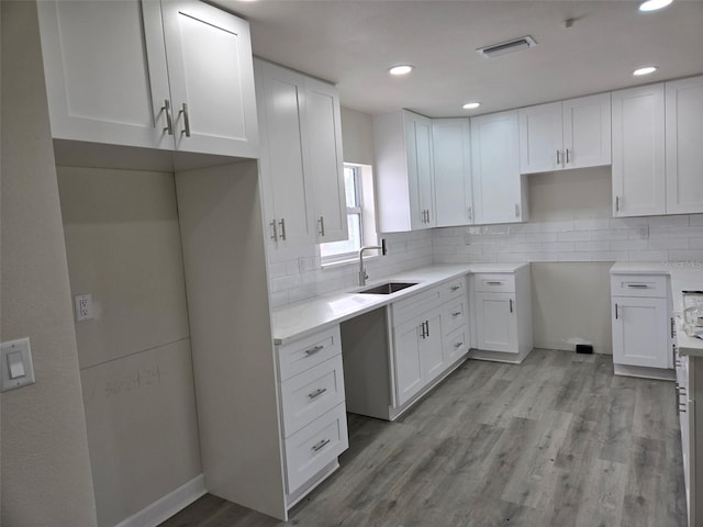 kitchen featuring visible vents, a sink, light wood-style flooring, and decorative backsplash