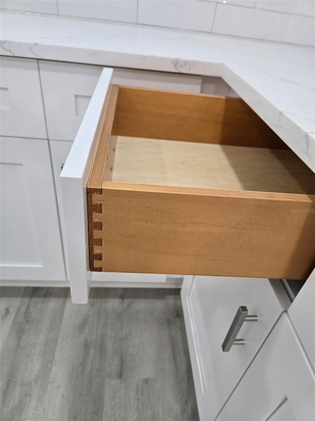 room details with light stone countertops, white cabinetry, and wood finished floors