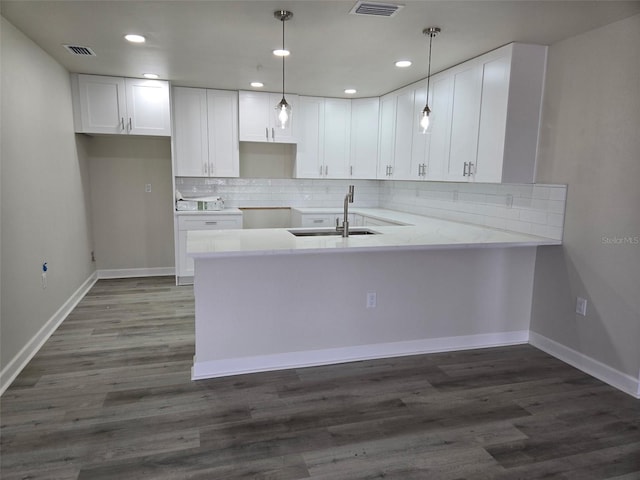 kitchen with decorative backsplash, dark wood-style floors, a peninsula, white cabinetry, and a sink