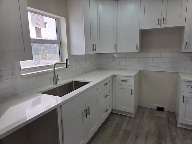 kitchen featuring light stone countertops, backsplash, white cabinetry, a sink, and wood finished floors