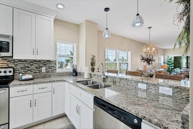 kitchen with kitchen peninsula, sink, light stone counters, hanging light fixtures, and appliances with stainless steel finishes