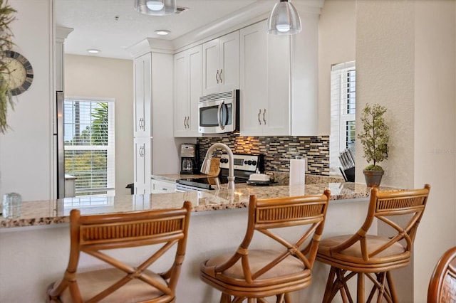 kitchen featuring light stone countertops, white cabinetry, backsplash, appliances with stainless steel finishes, and a breakfast bar