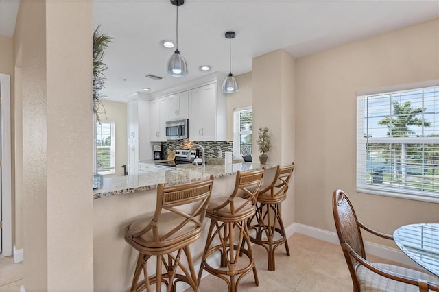 kitchen featuring pendant lighting, light tile floors, light stone countertops, appliances with stainless steel finishes, and white cabinetry