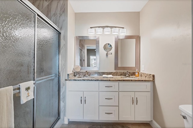 bathroom featuring double vanity, toilet, and a shower with door