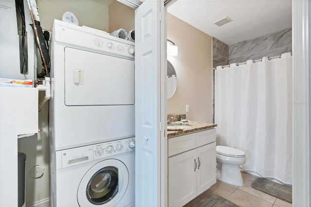 clothes washing area with stacked washer and clothes dryer and light tile floors