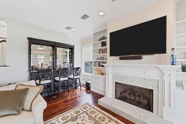 living room featuring bar area, a premium fireplace, crown molding, dark hardwood / wood-style floors, and built in shelves