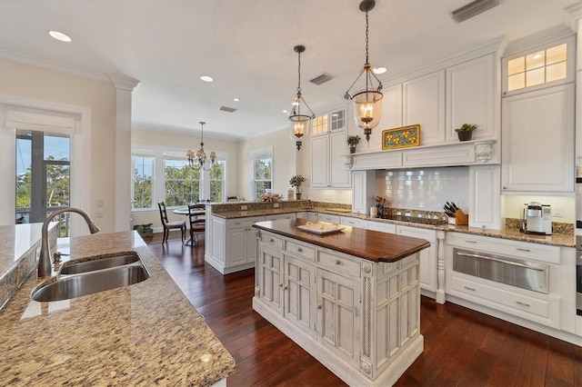 kitchen with dark hardwood / wood-style floors, a kitchen island with sink, sink, decorative light fixtures, and a notable chandelier