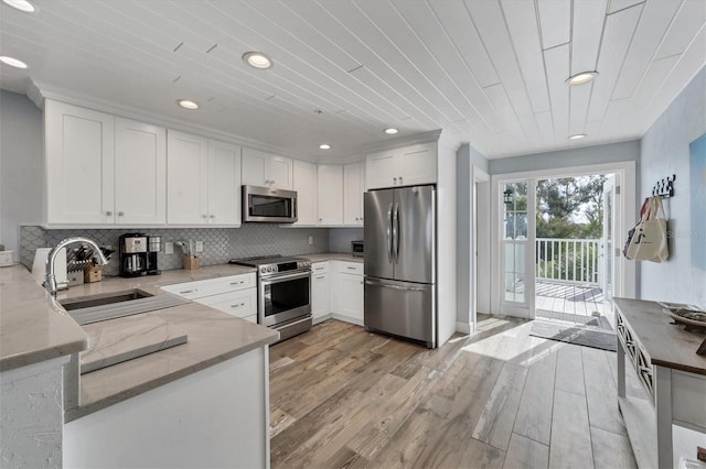 kitchen with appliances with stainless steel finishes, light hardwood / wood-style flooring, light stone counters, white cabinets, and sink