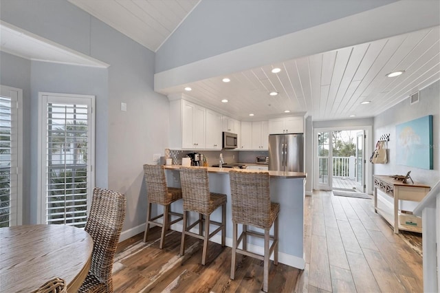 kitchen featuring white cabinets, hardwood / wood-style floors, backsplash, kitchen peninsula, and stainless steel appliances