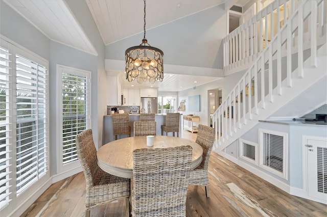 dining room with a chandelier, plenty of natural light, a towering ceiling, and light wood-type flooring