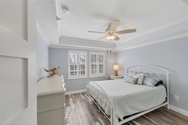 bedroom with dark hardwood / wood-style floors, ceiling fan, a tray ceiling, and ornamental molding