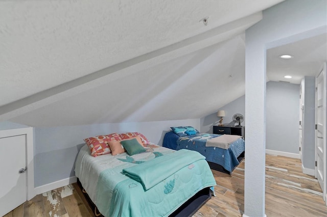 bedroom featuring lofted ceiling, light wood-type flooring, and a textured ceiling