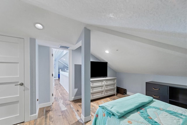 bedroom with lofted ceiling, light hardwood / wood-style flooring, and a textured ceiling