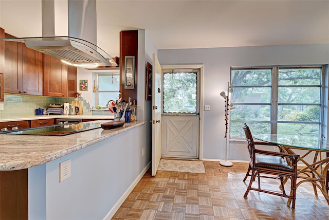 kitchen featuring light stone countertops, decorative backsplash, island range hood, and plenty of natural light