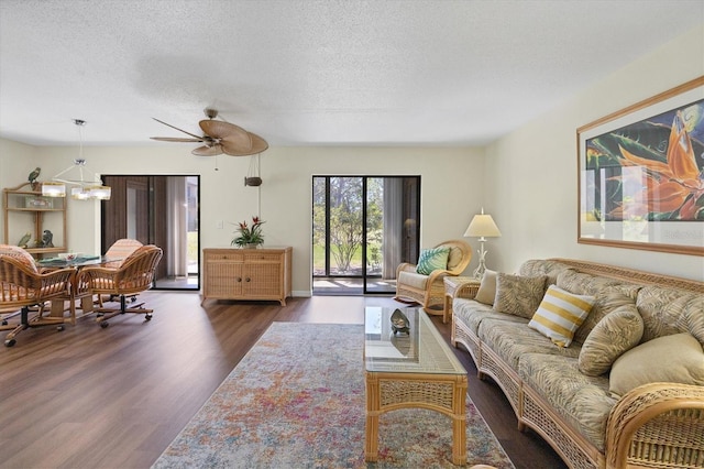 living room with a textured ceiling, dark wood-type flooring, and ceiling fan with notable chandelier