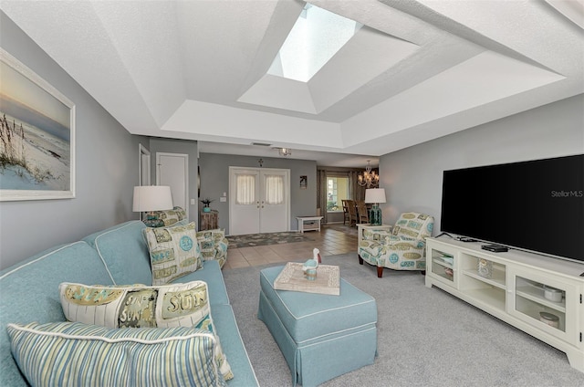 living room featuring a notable chandelier, a raised ceiling, light tile floors, a textured ceiling, and a skylight