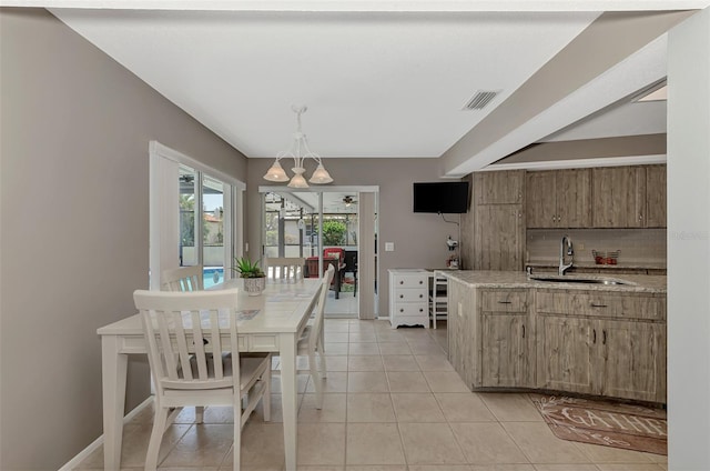 kitchen with hanging light fixtures, sink, light tile floors, and light stone counters