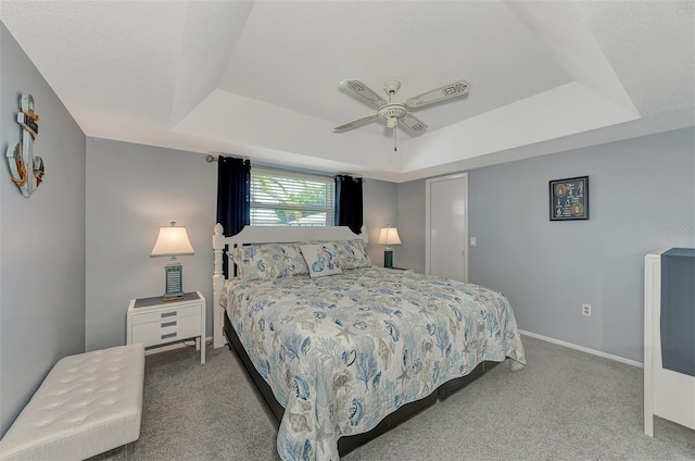 carpeted bedroom with ceiling fan and a tray ceiling