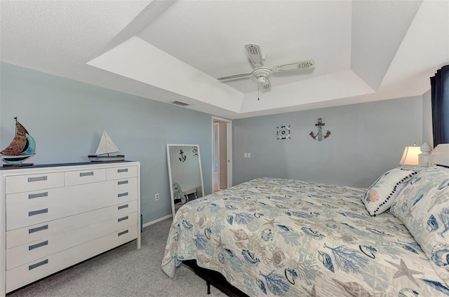 carpeted bedroom with ceiling fan, a tray ceiling, and a textured ceiling